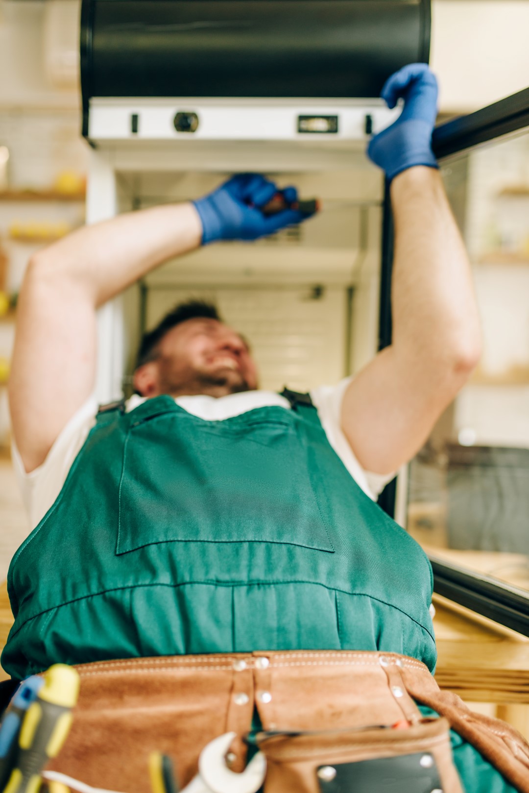 Worker in gloves repair refrigerator at home